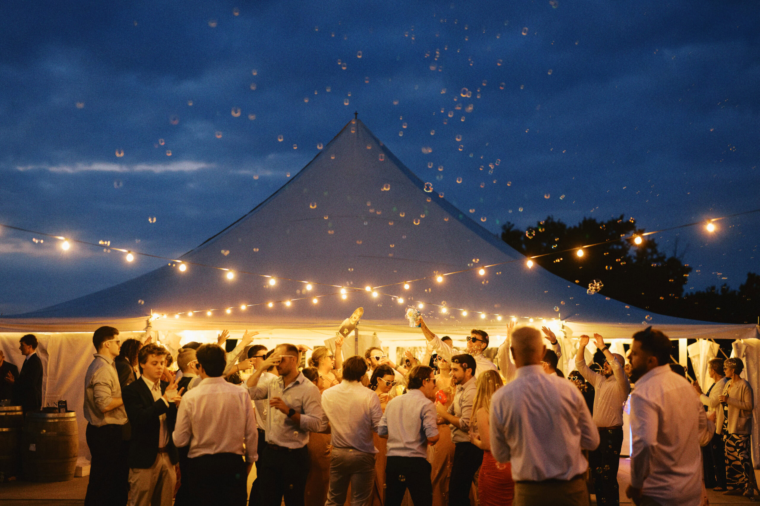 Festive outdoor wedding reception with guests dancing and celebrating under string lights.