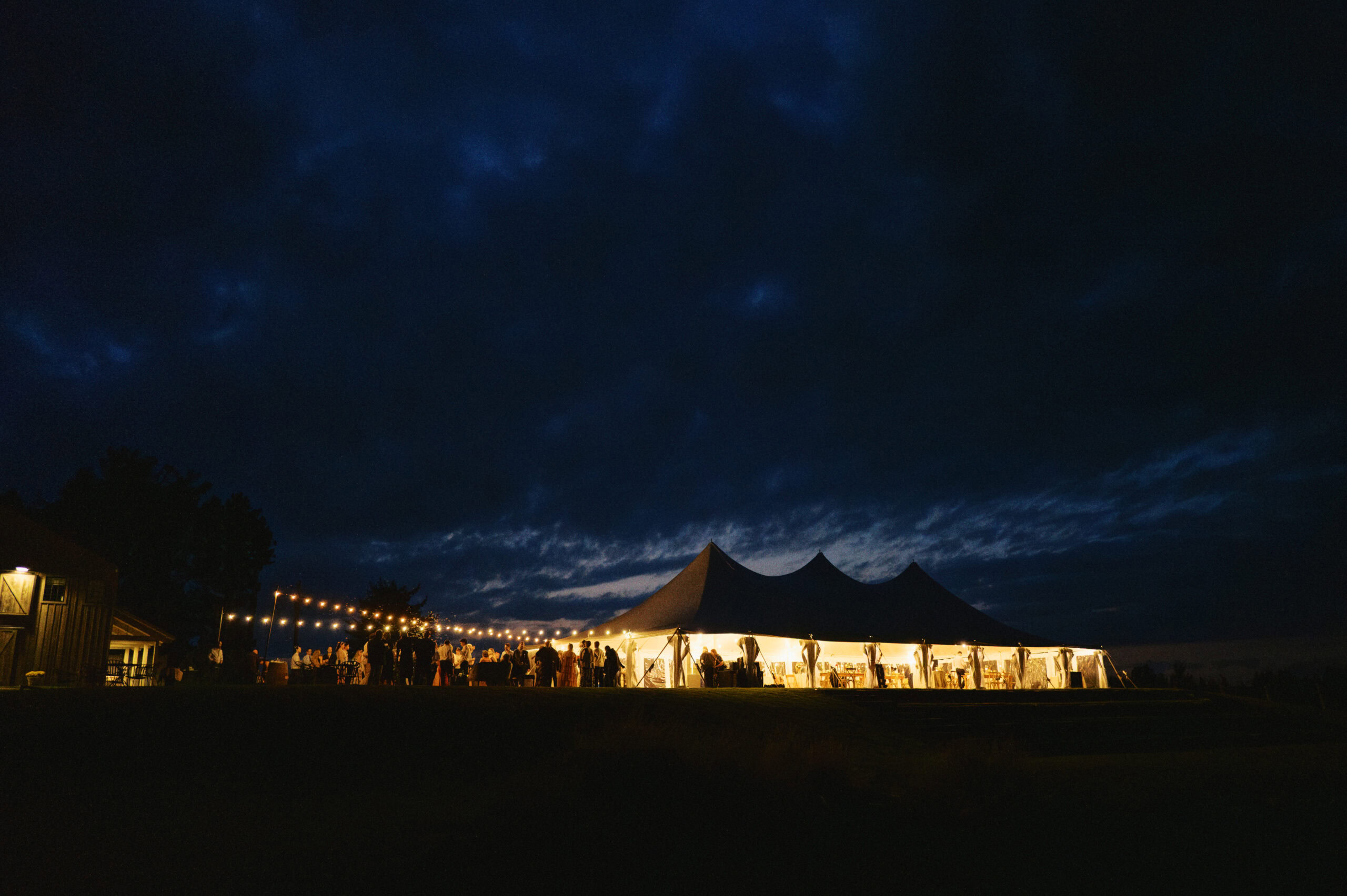 Wedding tent illuminated at night with string lights, set outdoors for a wedding reception.